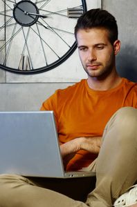 man with orange shirt using laptop